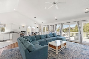 A spacious living room with a sectional sofa, a glass coffee table, and a view of the outdoors through large sliding glass doors. - Moon Over Magnolia: Private Pool, Spa, Rec Room (Corolla)