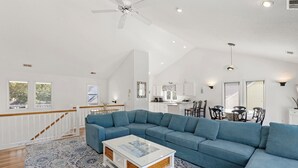 Una sala de estar amplia con un sofá seccional azul grande, una mesa de centro de vidrio y una escalera con barandilla de madera.