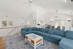 A spacious living room with a large blue sectional sofa, a glass-top coffee table, and a staircase with a wooden railing.