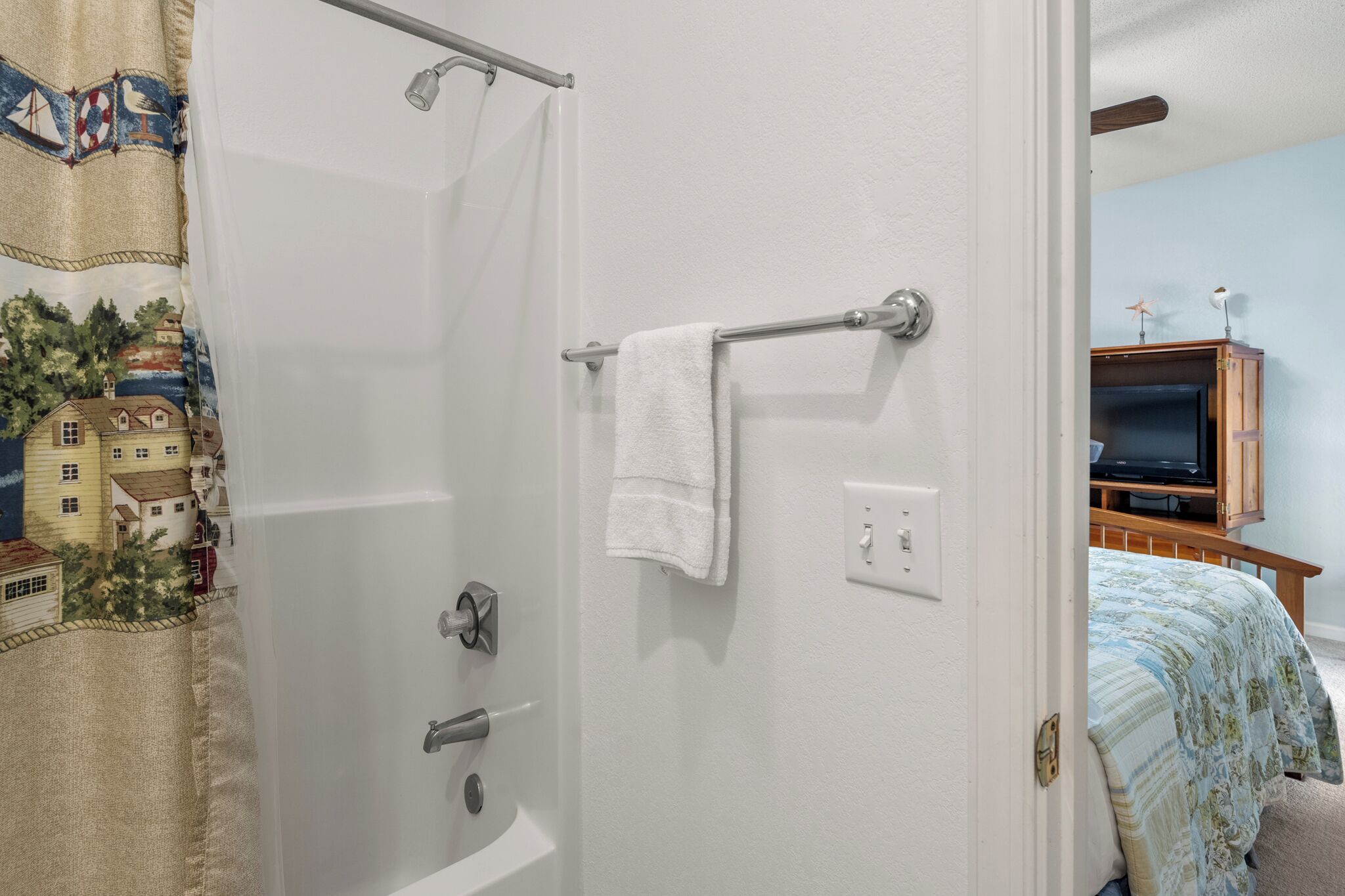 Un bagno con una vasca da bagno bianca, un appendi asciugamani con un asciugamano bianco e un armadietto in legno con un televisore.