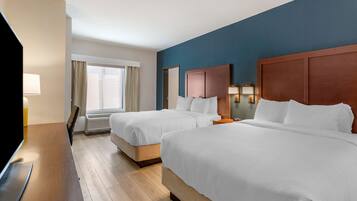 A hotel room with two beds, a TV, a desk, and a window with curtains.