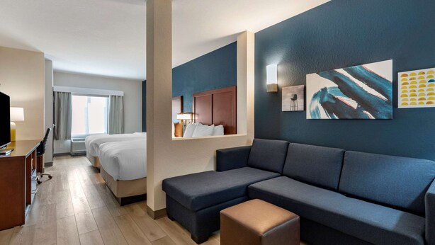 A hotel room with a sofa, a desk, a bed, and a large window.