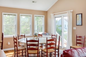 A dining area with a round table surrounded by wooden chairs, large windows, and a view of the outdoors.