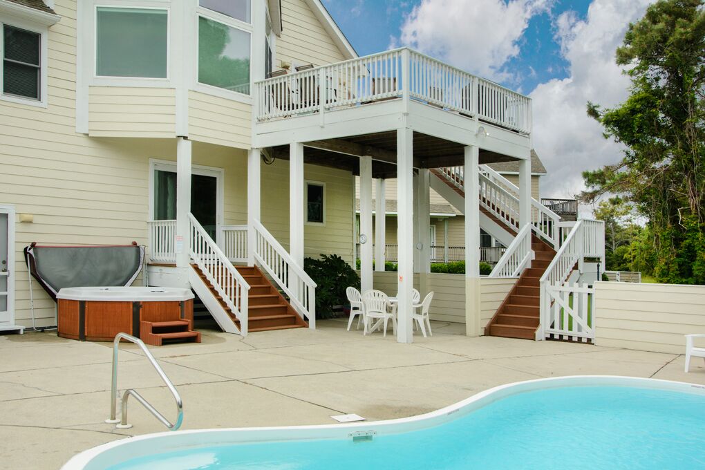Ein zweistöckiges Haus mit überdachter Terrasse, Whirlpool und Schwimmbad.
