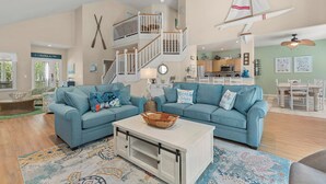 A spacious living room with two blue sofas, a white coffee table, and a staircase with a railing.