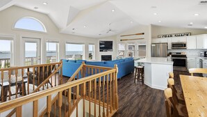 A spacious living area with a blue sectional sofa, wooden staircase, and a kitchen with white cabinets and stainless steel appliances. - Soundset : Soundview Private Spa, Golf, Share Pool (Nags Head)