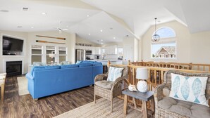 A spacious living area with a blue sofa, wicker furniture, and a fireplace. - Soundset : Soundview Private Spa, Golf, Share Pool (Nags Head)