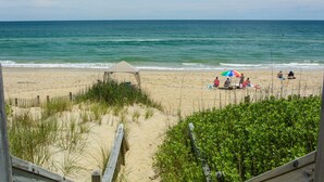 Una platja amb una tanca de fusta, una ombrelló de platja i gent relaxant-se a la sorra.
