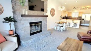 Una sala de estar con chimenea, comedor y cocina al fondo.
