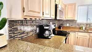 Una cocina con encimeras de granito, cafetera, fregadero y una planta de cactus.