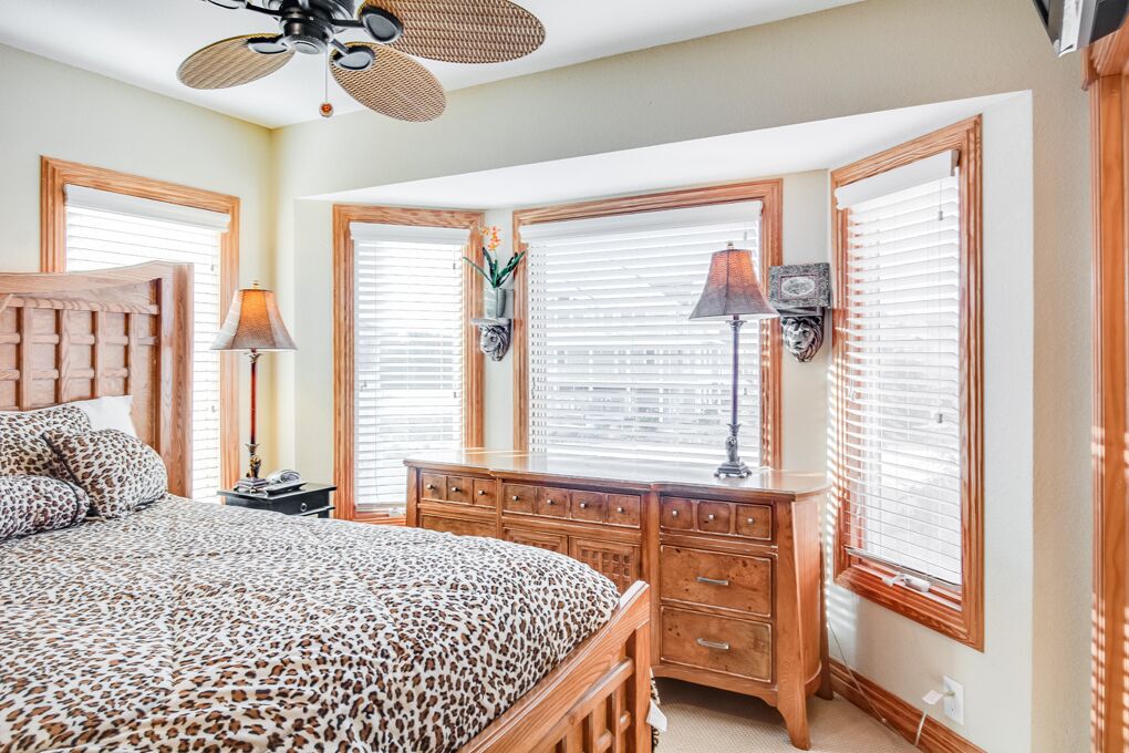A bedroom with a bed, wooden dresser, and two windows with blinds.