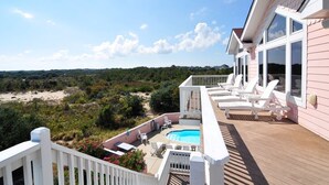Ein pinkfarbenes Haus mit einer Terrasse, einem Pool und weißen Stühlen.