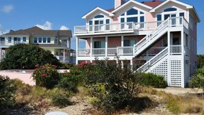 Ein Strandgrundstück mit einem mehrstöckigen Haus, das Balkone und eine Treppe hat.