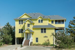 A two-story yellow house with a front porch, a staircase, and a small front yard. - Seaduction: Oceanside, 6-bedrooms, Private Pool & Hot Tub, 3 lots from the ocean (Corolla)