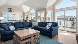A spacious living room with a large sectional sofa, a wooden coffee table, and a view of the ocean through large windows. - Fish Tank: Oceanside, Private Pool, Hot Tub, close to beach & golf discounts! (Corolla)