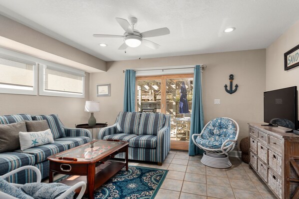 A living room with striped sofas, a glass coffee table, a wicker chair, and a wooden cabinet.