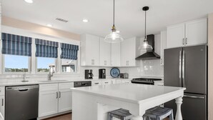 A modern kitchen with white cabinets, stainless steel appliances, and a large island with stools. - Fish Tank: Oceanside, Private Pool, Hot Tub, close to beach & golf discounts! (Corolla)