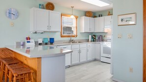 Een moderne keuken met witte kastjes, een centraal eiland met krukken, een ingebouwde oven en een raam met zonwering.
