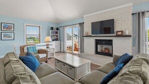 Un salon avec une cheminée en briques blanches, un téléviseur à écran plat et une grande fenêtre donnant sur l’extérieur.