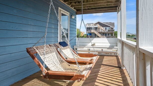 Une terrasse en bois avec deux fauteuils en osier et un banc blanc.