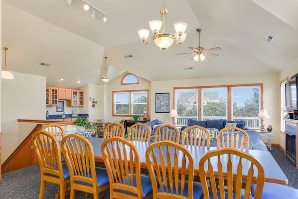 A spacious dining area with a long table and wooden chairs, a chandelier, and a ceiling fan.