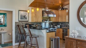 Een moderne keuken met houten kasten, een centraal eiland met krukken, roestvrijstalen apparatuur en hangende lampen.
