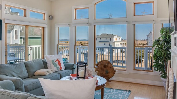 Een ruime woonkamer met een groot raam met uitzicht op een strand en een huis.