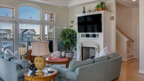 Een ruime woonkamer met een open haard, comfortabele zithoek en grote ramen met uitzicht op zee.