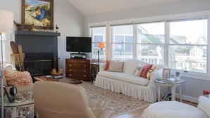 Una sala de estar con chimenea, televisor y ventanas amplias que ofrecen vistas al exterior.