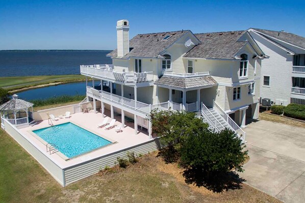 A large house with a swimming pool, a covered deck, and a view of the ocean.