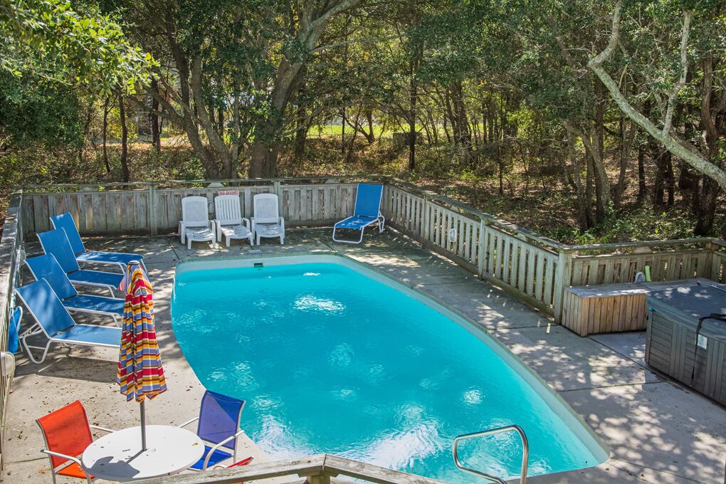 A rectangular swimming pool with blue water, surrounded by a wooden deck and a wooden fence.