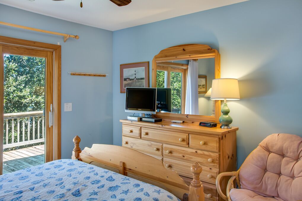A bedroom with a bed, wooden dresser, television, and a large mirror.