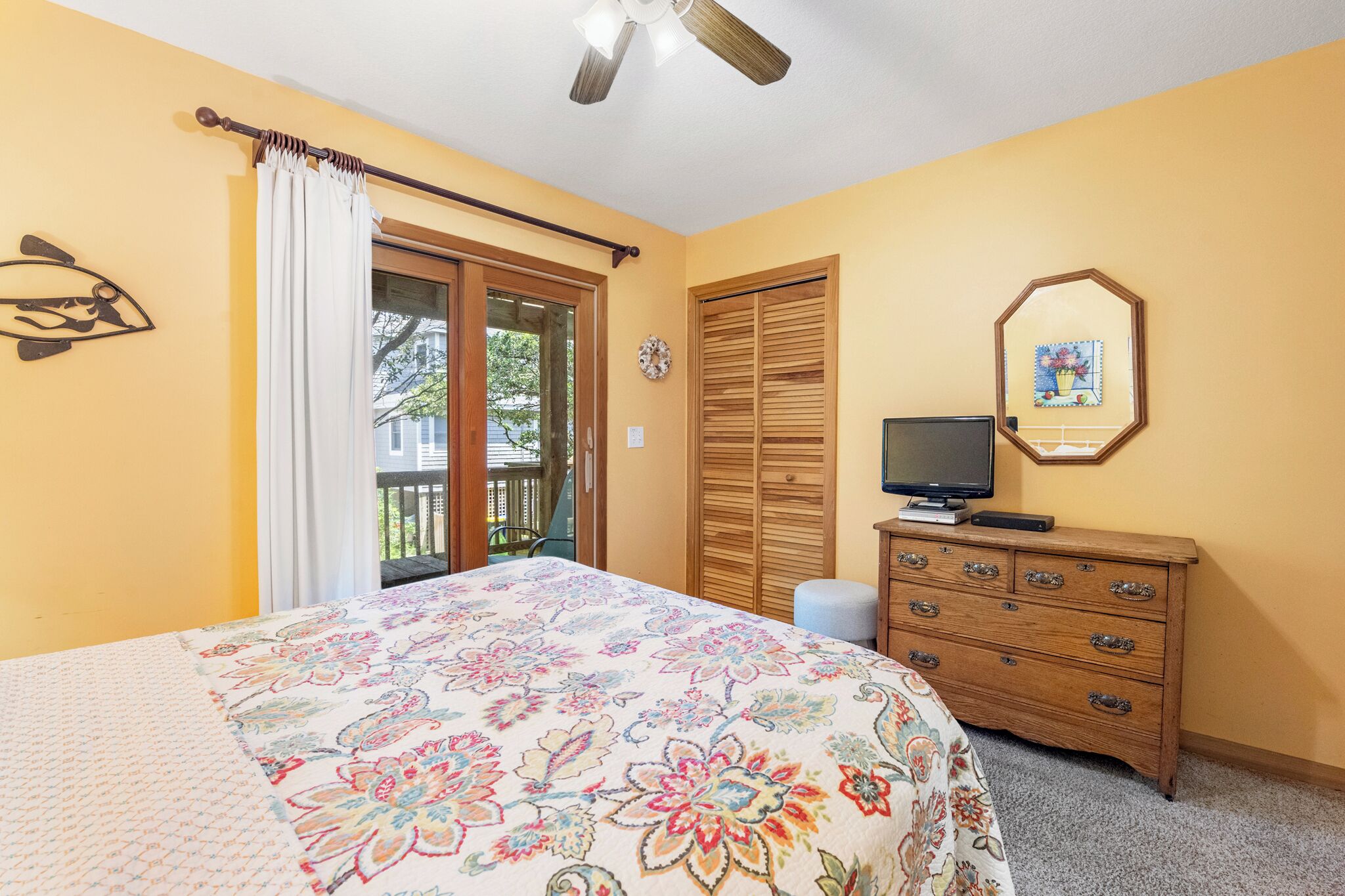 Une chambre à coucher avec un lit, une commode, un téléviseur et une fenêtre avec des rideaux.