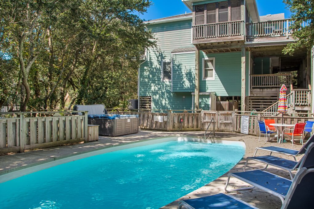 A pool area with a wooden deck, lounge chairs, and a hot tub.