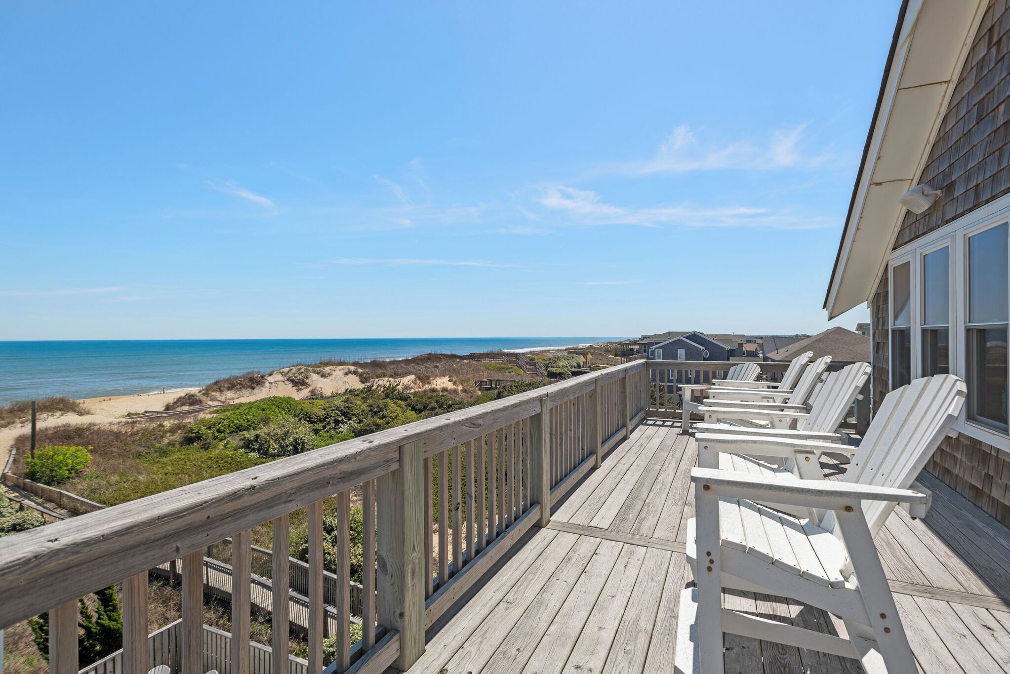 A wooden deck with white chairs overlooking a beach and ocean.