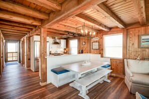L’intérieur d’un chalet en bois comprend une table à manger centrale, des bancs, un coin cuisine et un espace salon confortable.