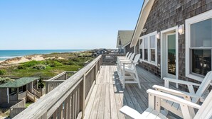 A wooden deck with white chairs overlooking a beach. - Cobia: Oceanfront Home w/ Private Heated Pool, Hot Tub & Cabana Service (Nags Head)