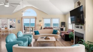 A spacious living room with a large TV, comfortable seating, and a view of the ocean. - Turtles Roost: Oceanfront, Pool, Spa, Game room (Nags Head)