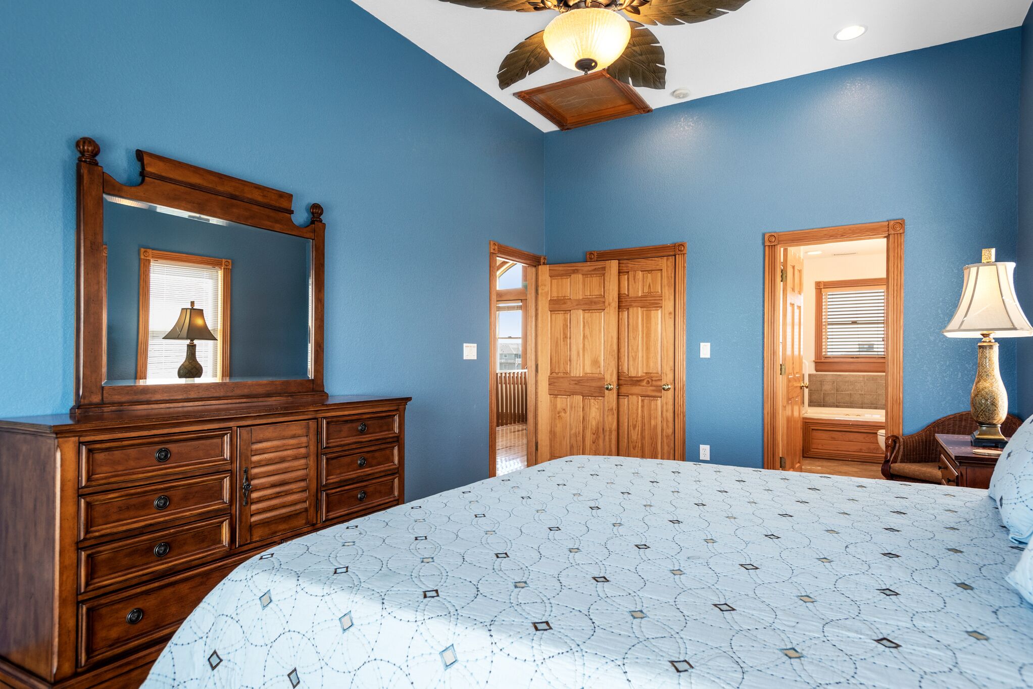 Quarto com cama grande, cômoda de madeira e ventilador de teto.