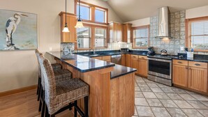 A kitchen with a central island, wooden cabinets, a stainless steel range, and a large window with blinds. - Salt Shaker: Semi-oceanfront, Private Pool, Spa (Nags Head)