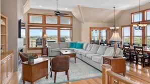 A spacious living room with a large sectional sofa, a wooden coffee table, and a dining area with a chandelier. - Salt Shaker: Semi-oceanfront, Private Pool, Spa (Nags Head)