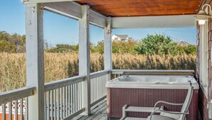 Une terrasse en bois avec un jacuzzi et des chaises, donnant sur un champ verdoyant et des maisons.