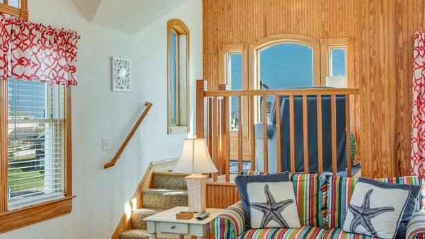 Un salon chaleureux avec un mur d’accent en bois, un canapé à rayures et un escalier menant à un niveau supérieur.