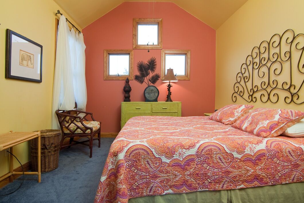 Une chambre à coucher comprenant un lit, un bureau, une chaise, une commode et trois fenêtres.