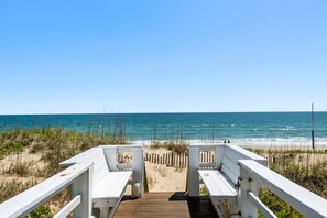 A wooden deck leading to a beach with white railings and benches.