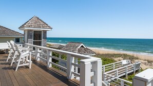 A wooden deck with white railings overlooking a beach.