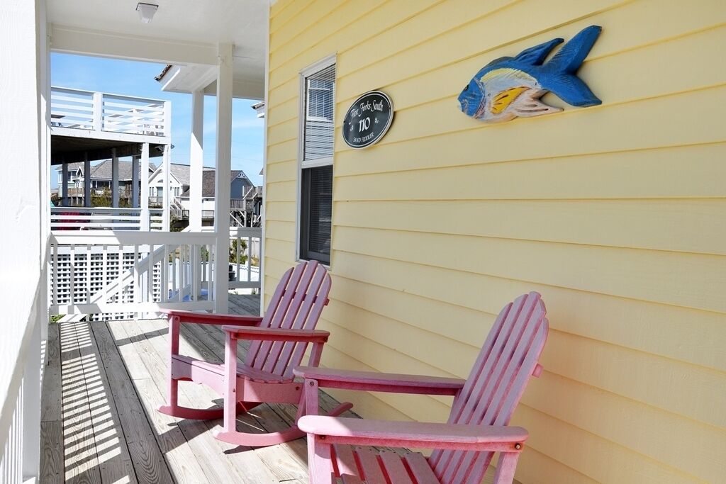 A porch with two pink Adirondack chairs, a white railing, and a blue fish decoration on the wall.