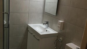 Une salle de bain avec une douche à parois de verre, un lavabo blanc avec un miroir au-dessus et des toilettes.