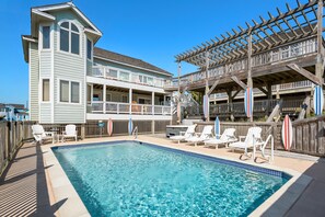 Un espace piscine avec un bâtiment à deux étages, une terrasse en bois et des chaises longues.