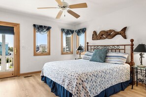 Une chambre avec un lit, un ventilateur de plafond, un décor mural représentant des poissons et une vue par la fenêtre.